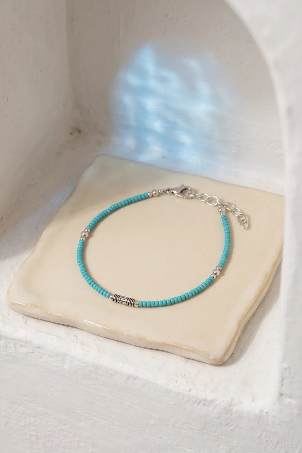 Pulsera de turquesa azul con pequeñas cuentas redondas, cierre plateado y cadena ajustable sobre una base de piedra clara.