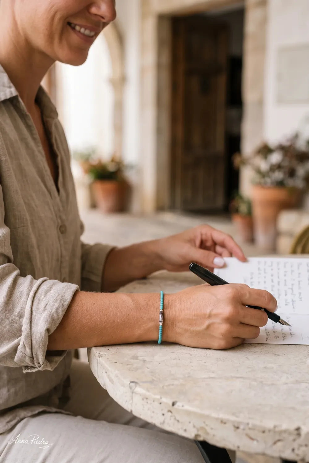 Mujer escribiendo en un cuaderno mientras lleva una pulsera de turquesa azul con adorno central plateado.