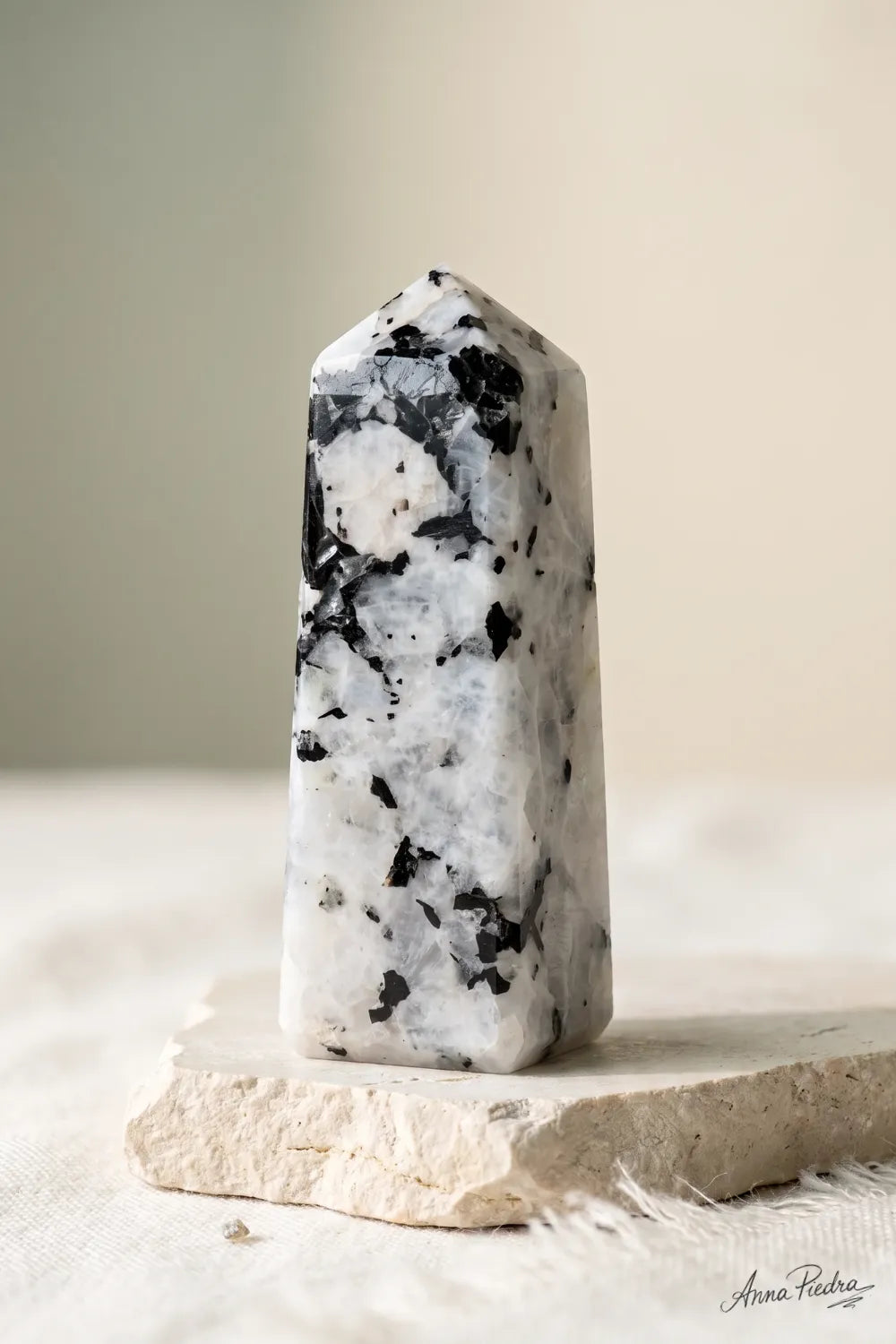 Punta de piedra luna pulida en tonos blancos y negros, fotografiada sobre una base de piedra clara