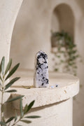 Punta de piedra luna pulida de color blanco con vetas negras, colocada sobre una mesa de piedra clara