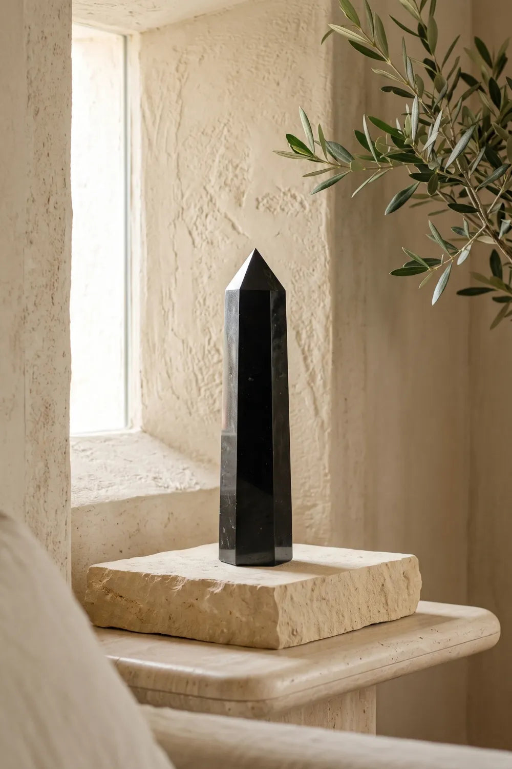 Torre de turmalina negra grande expuesta sobre una base de piedra beige en un ambiente sereno con luz natural.