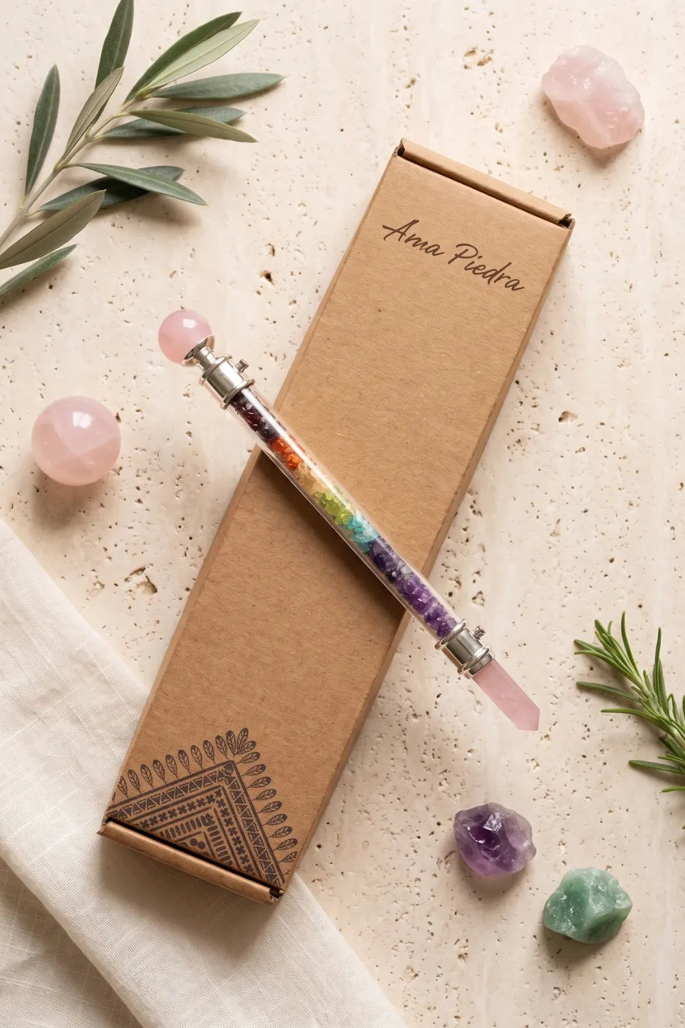 Varita de chakras con cuarzo rosa junto a su caja Anna Piedra y varias piedras naturales. anna piedra