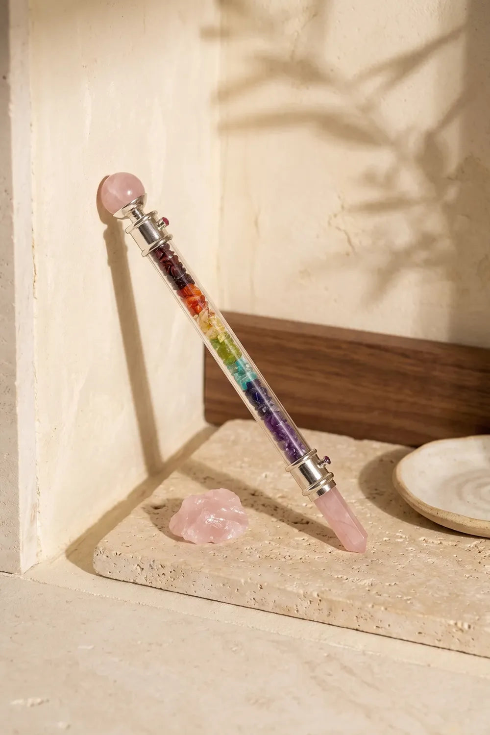 Varita de chakras con siete piedras naturales y cuarzo rosa apoyada sobre una superficie de piedra clara. anna piedra