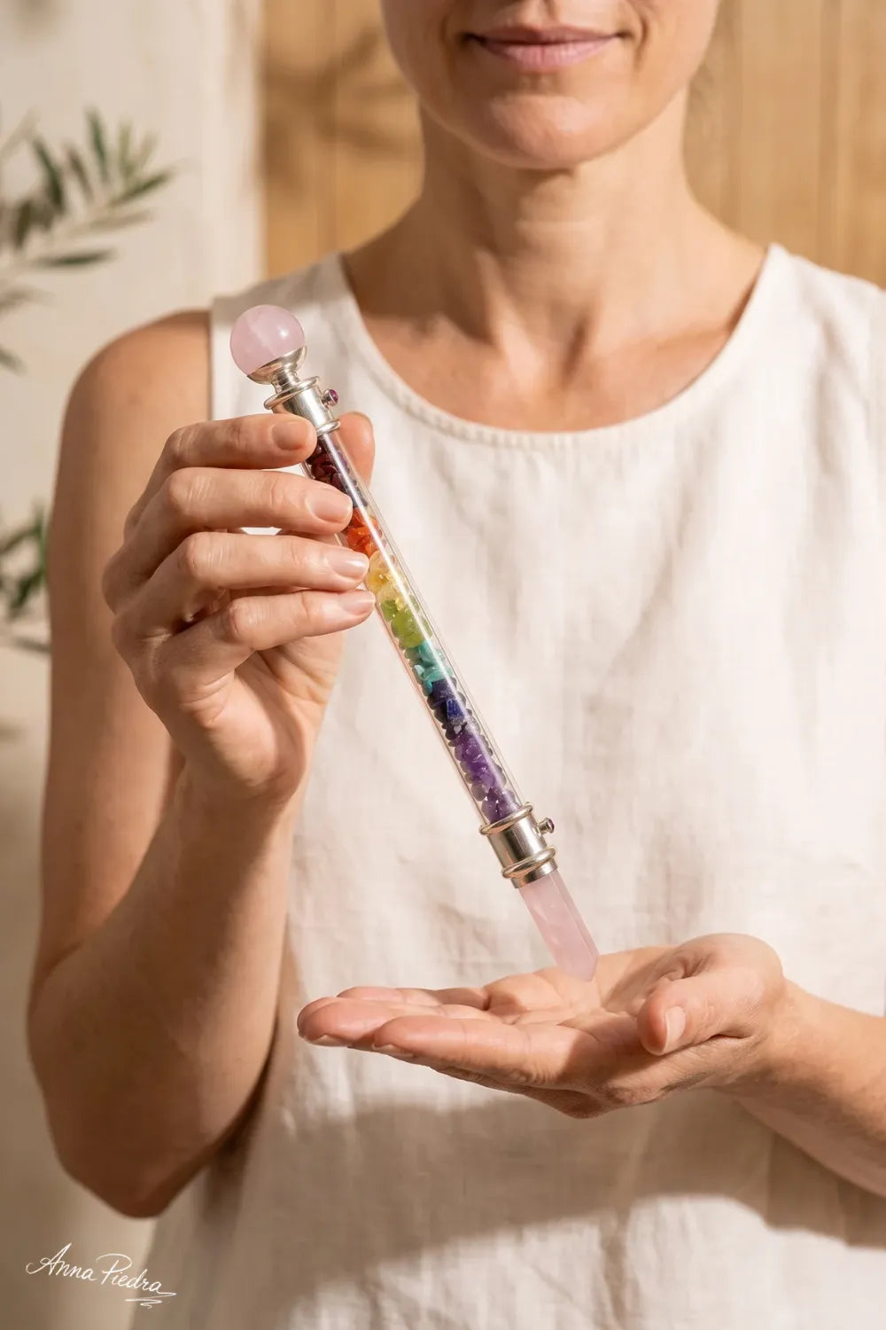 Detalle de una mujer sosteniendo una varita de chakras con cuarzo rosa y piedras naturales de colores. anna piedra